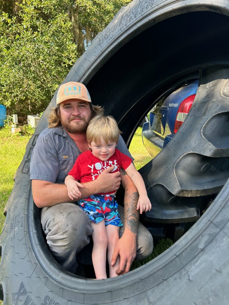 Central Florida Tire's owner holding his young son inside a large tractor tire